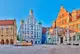 Panoramaaufnahme eines Marktplatzes mit historischen, verzierten Häusern und einem Brunnen.