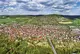 Luftaufnahme einer kleinen Stadt mit vielen Häusern und Straßen, darum herum Felder und Wälder.