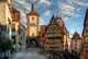 Fachwerkhäuser, eine Gasse mit Pflastersteinen und ein Turm mit Torbogen unter malerischem Himmel.