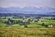 Landschaft mit Wiesen, Bäumen, ein paar Häusern und Bergen im Hintergrund.