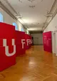 Flur mit Parkettboden und Stuckdecke, links sechs große rote Elemente mit weißen Lettern UFFRUR darauf.
